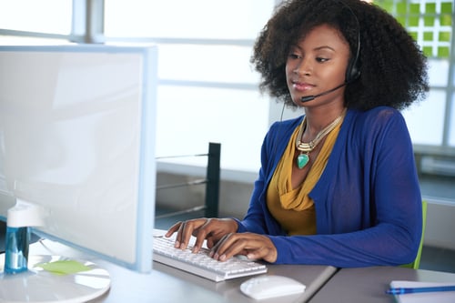 Portrait of a smiling customer service representative with an afro at the computer using headset-1